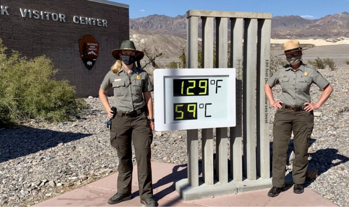 National Park Service rangers beside the Furnace Creek thermometer in Death Valley reading 129F