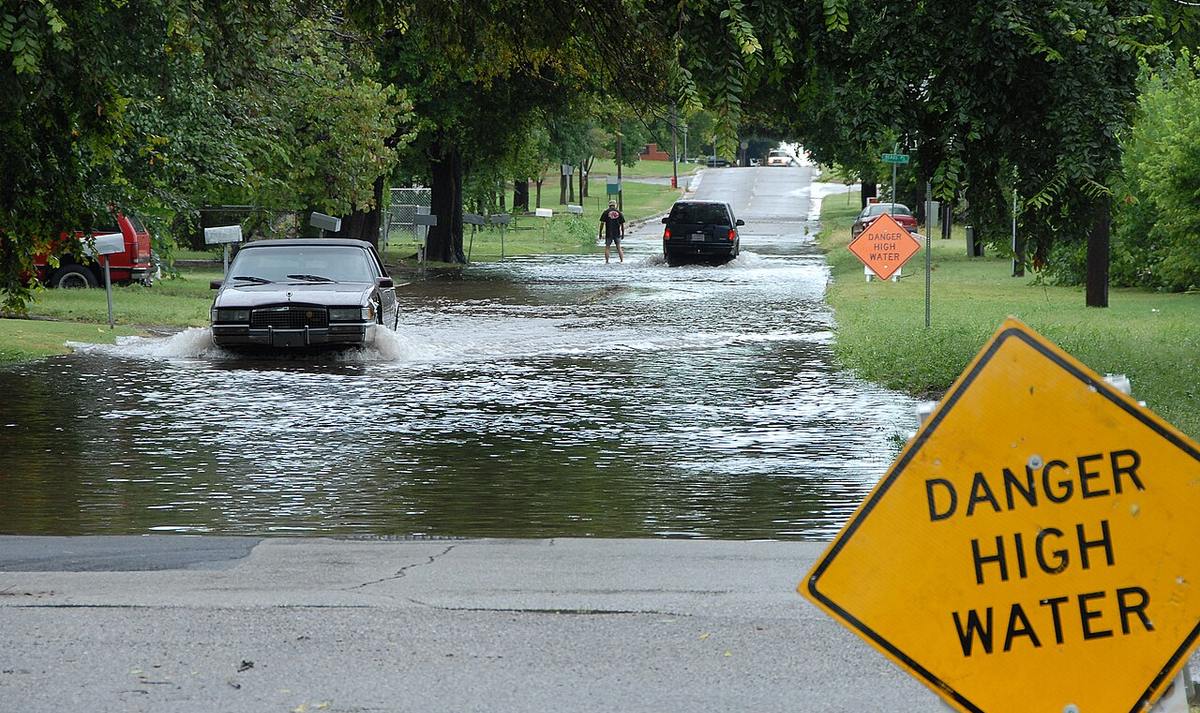Vehicles driving through flood water past a DANGER HIGH WATER sign on a residential street in Oklahoma