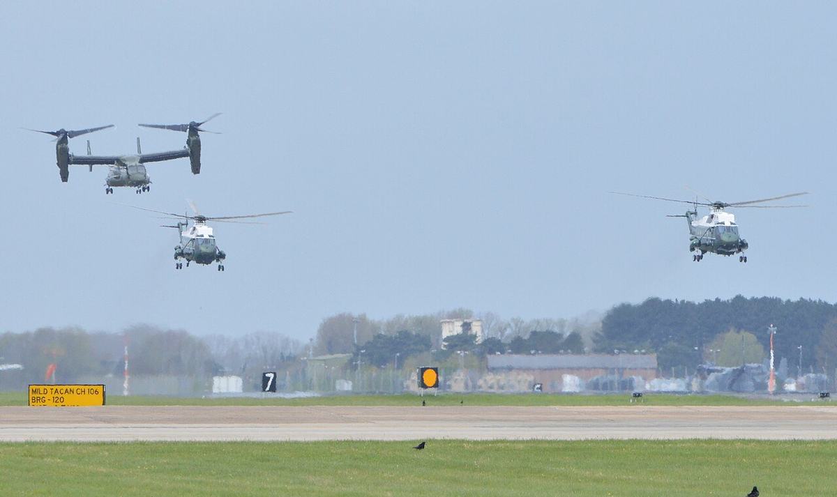 Two identical white-topped presidential helicopters flying in formation with a tiltrotor aircraft