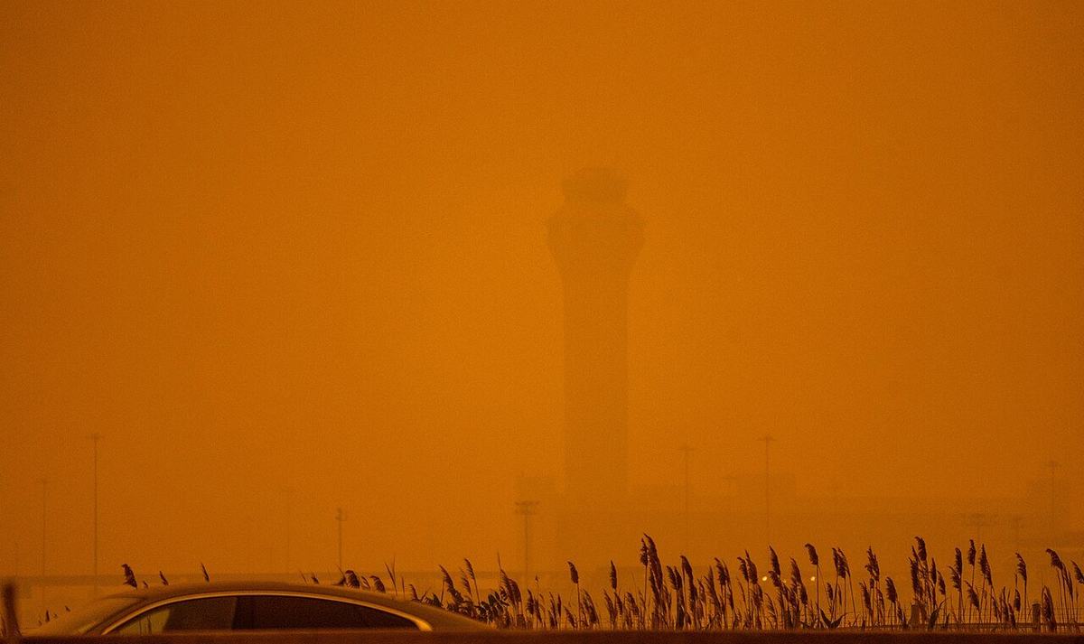 An airport control tower barely visible through thick orange wildfire smoke